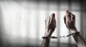 two hands in handcuffs against a light background