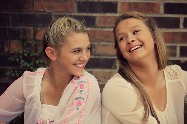 Two teenage girls sitting side by side and laughing.