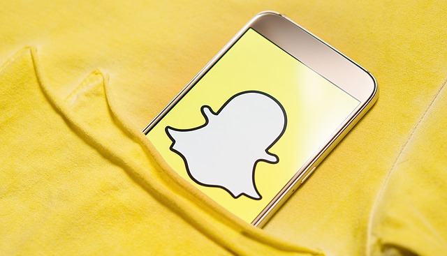 A close up of a smart phone in someone's pocket, showing the Snapchat logo on the screen.