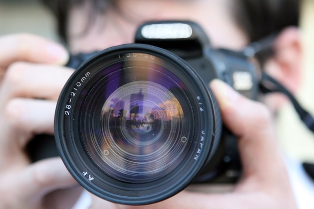 A close up of a man's face, partially obscured by a camera. He is taking pictures of someone.