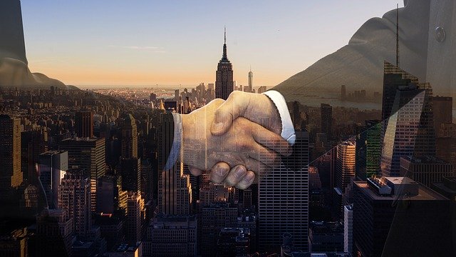A close-up of two men shaking hands. Their hands are super imposed over a view of a very big city.