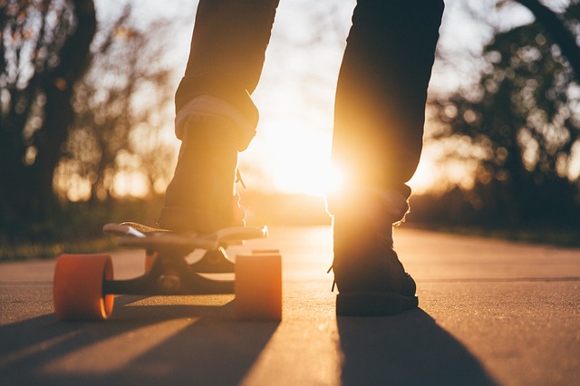 A close up of a teenager's feet, standing on a sidewalk at sunset with a skateboard.