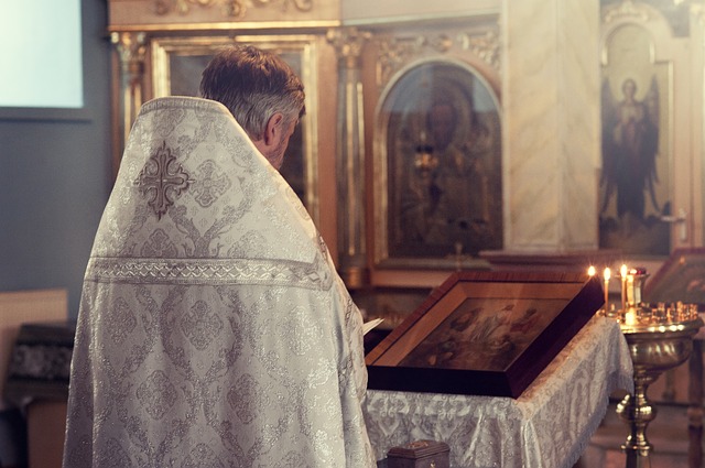 A priest standing at an altar in a Catholic church. His back is to the camera so you cannot see his face.