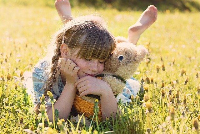 A young girl lying in a filed with her teddy bear.