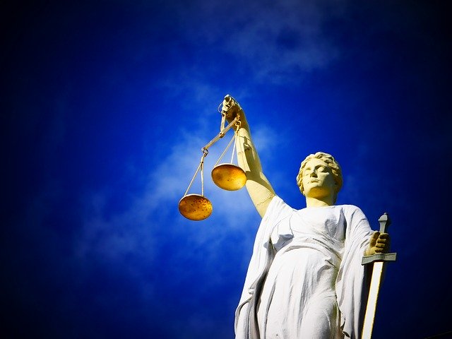Lady Justice holding up a pair of golden scales in front of a blue sky
