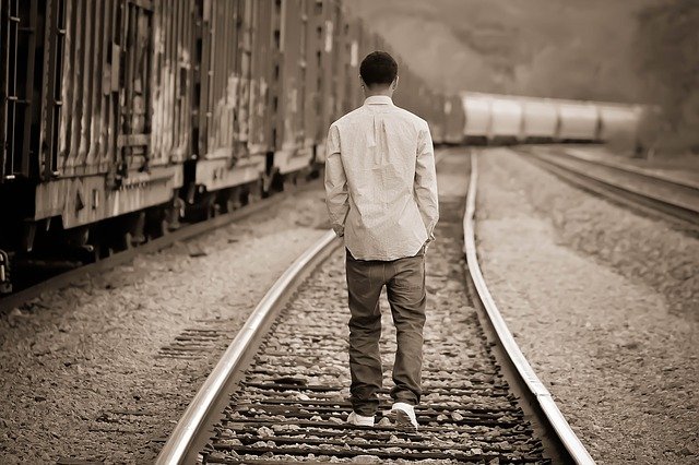 A young teen boy walking away from the camera down a train track. The piture is sepia toned, giving it a slightly sad appearance.