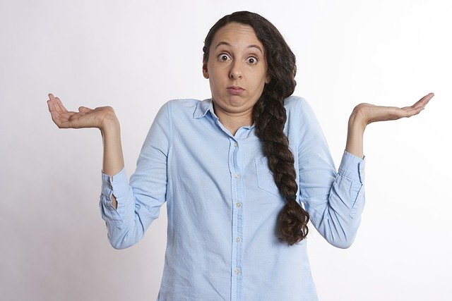 A woman with her hands in the air, and a confused look on her face, shrugging as if she doesn't understand something.